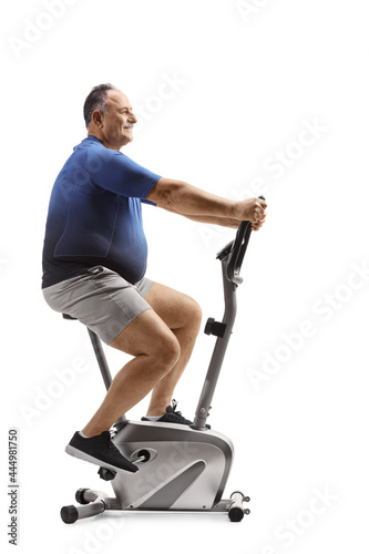 Full length profile shot of a corpulent mature man riding a stationary bike