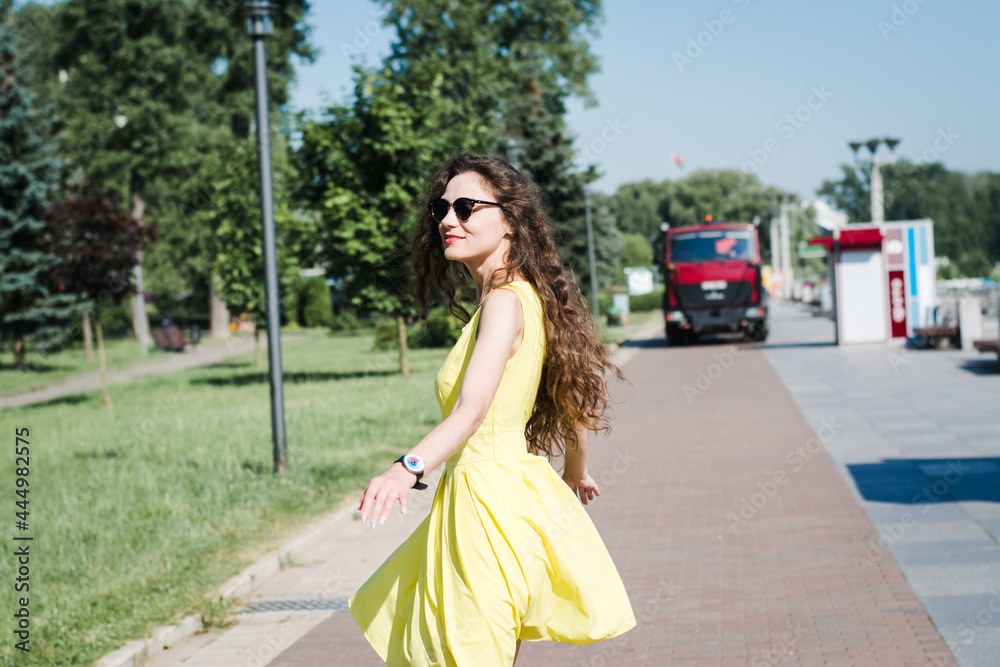 Beautiful girl in a yellow dress walks in a summer park