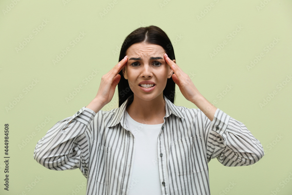 Woman suffering from migraine on light green background Woman suffering from migraine on light green background