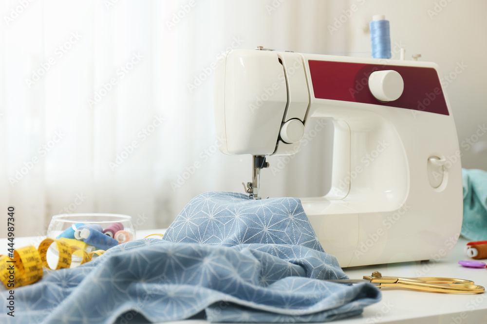 Modern sewing machine, fabric and accessories on table indoors