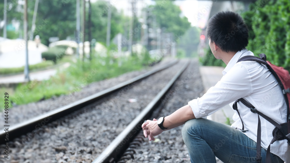 Fototapeta premium Alone man sit on along a railway track to meet a train. vacation concept.