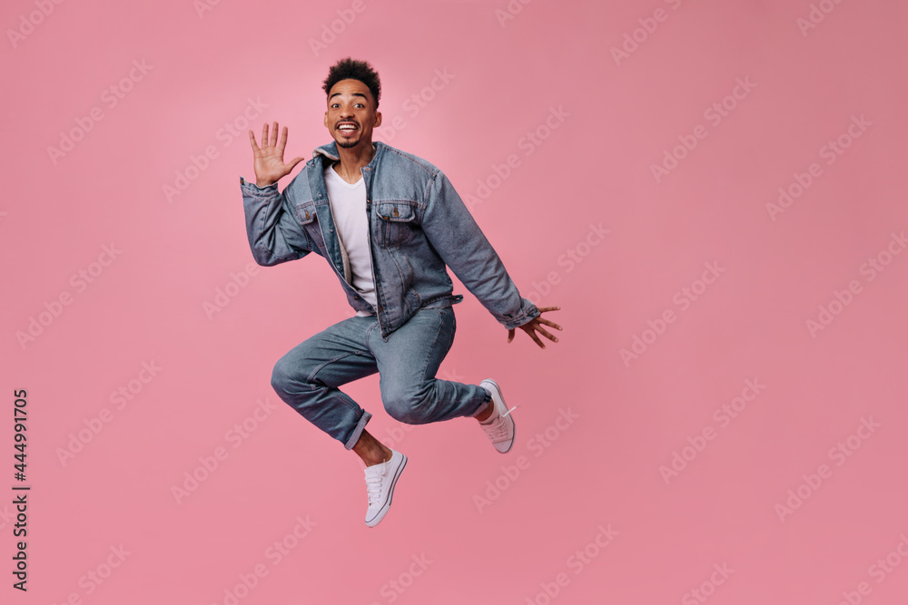 Cheerful man in jeans and denim jacket jumping on pink background. Cool guy in blue outfit move on isolated backdrop Cheerful man in jeans and denim jacket jumping on pink background. Cool guy in blue outfit move on isolated backdrop