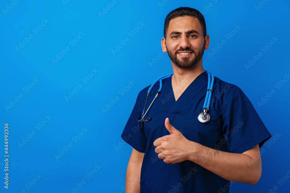 Handsome young male doctor in blue uniform with stethoscope against blue background Handsome young male doctor in blue uniform with stethoscope against blue background