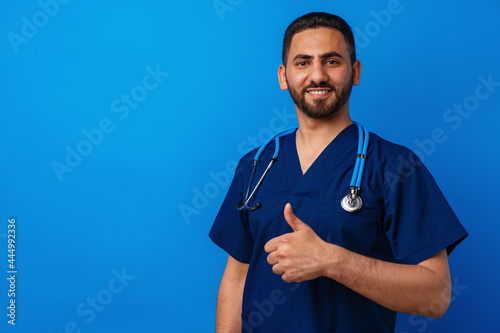 Handsome young male doctor in blue uniform with stethoscope against blue background
