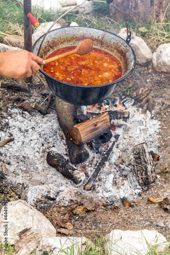 Metal cauldron boiling on a bonfire. Cooking on open fire, camping meal. Traditional preparation of goulash on a campfire Metal cauldron boiling on a bonfire. Cooking on open fire, camping meal. Traditional preparation of goulash on a campfire