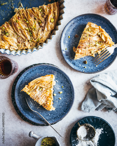An Egyptian Phyllo Milk Pie (Um Ali) plated on blue dishes, served with coffee and garnishes of pistachio and confectioner's sugar photo