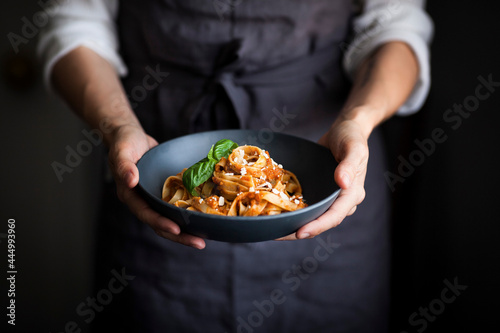 A blue bowl of pasta and tomato sauce held by a cook photo