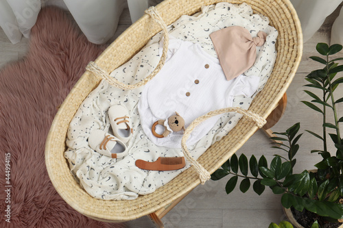 Fotografie Cute baby clothes and accessories in basket bassinet at home, top view