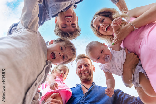 shot from below of a young adult family time having fun outdoors. mom and dad portrait carrying kids on holiday with children. cropped low view of happy people. joy, togetherness and lifestyle concept photo