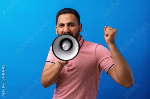 Young arab man with megaphone proclaiming something isolated on blue background