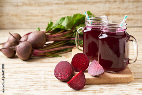 Fresh beet juice in a mason jar glases and vegetables on a wooden table.