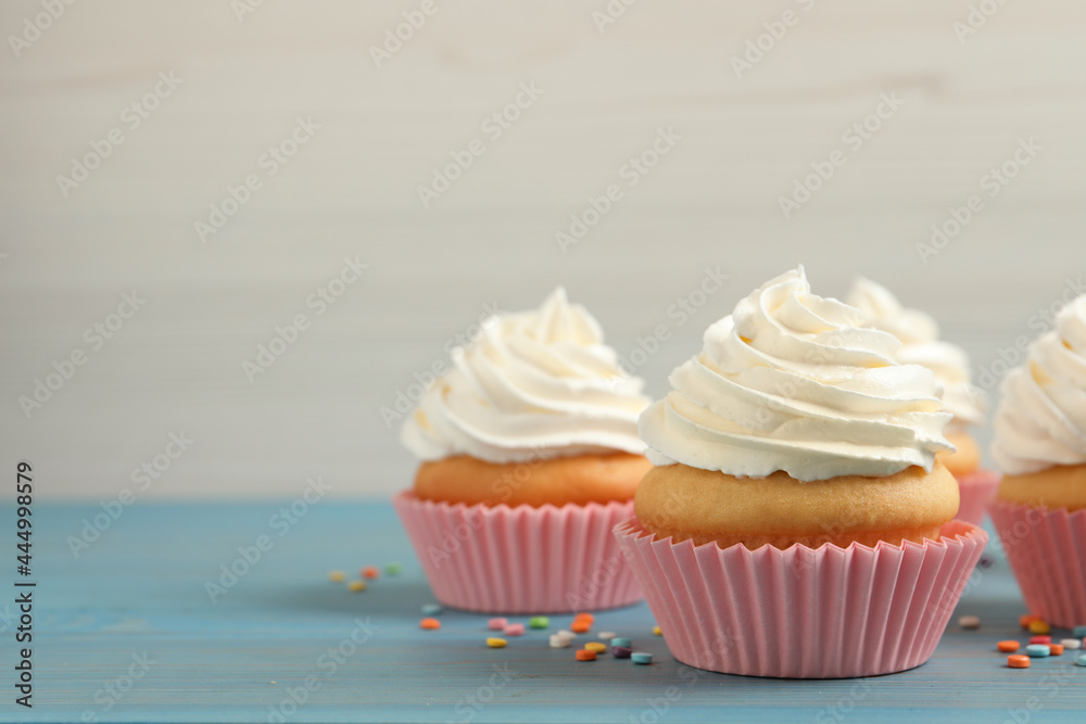 Delicious cupcakes decorated with cream on light blue wooden table, space for text