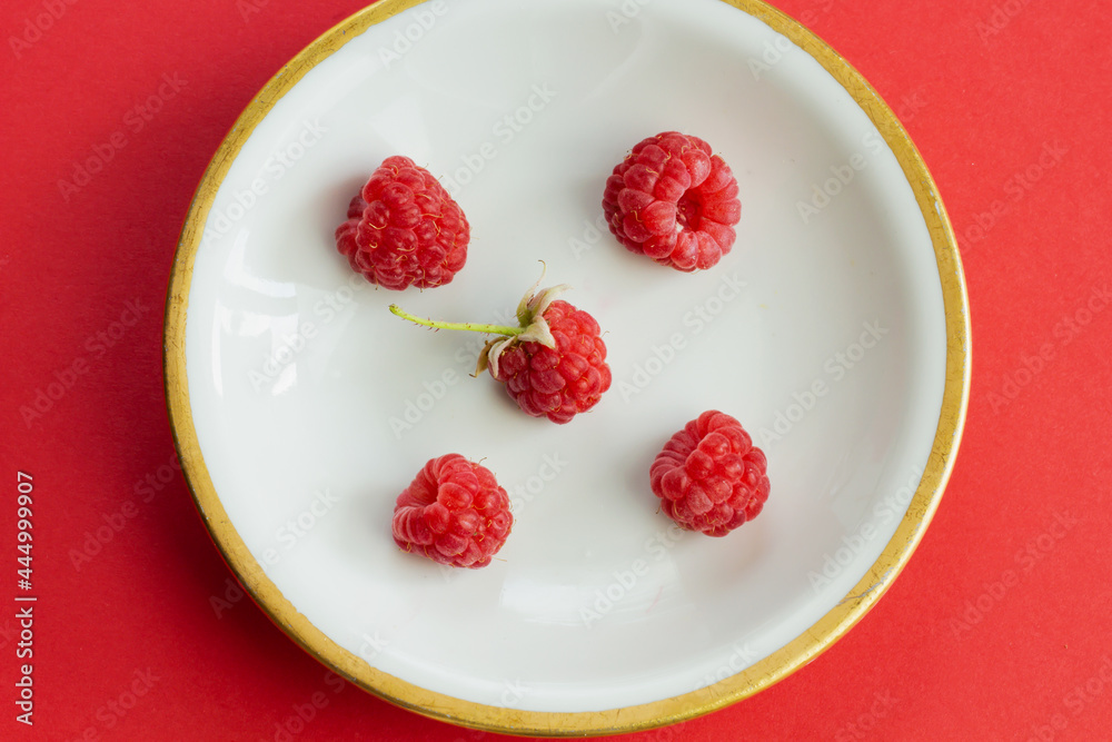 Ripe organic raspberry berry on plate, healthy pile of summer berries  top view. Pattern flat lay of scarlet  raspberry on red background