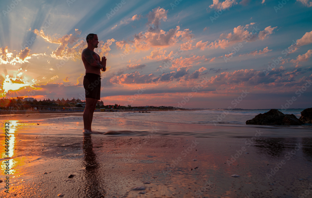 Ein Mann bei Morgenstunde im Sonnenaufgang am Meer beim meditieren