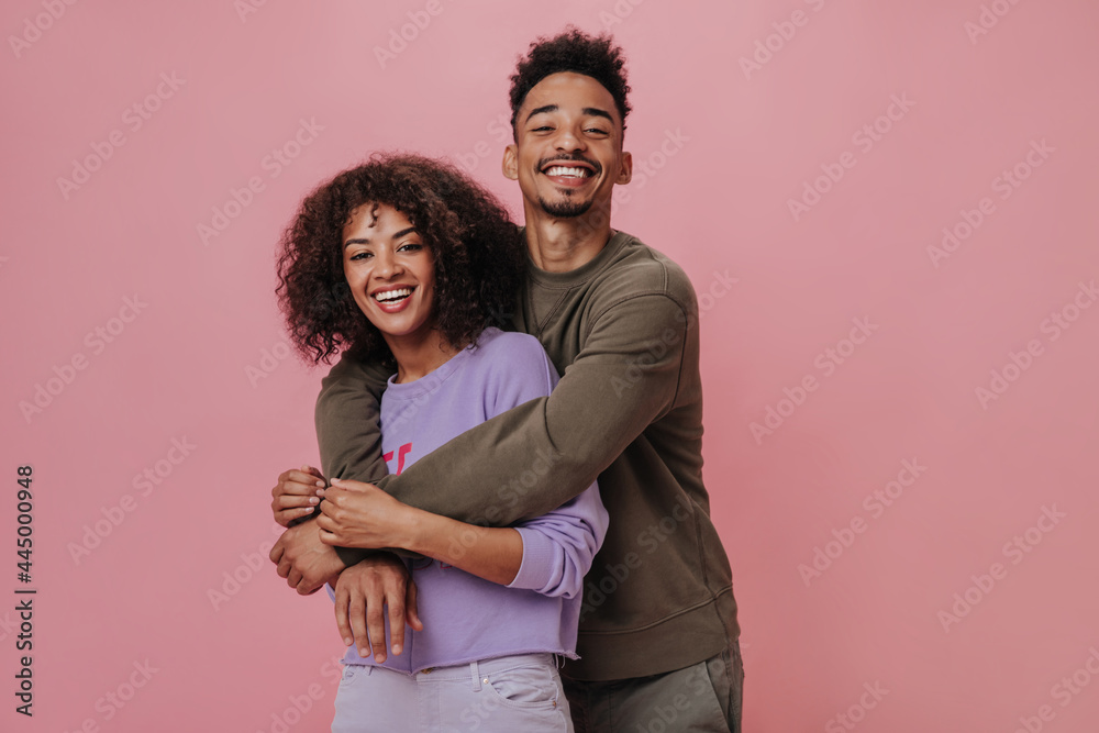Portrait of happy couple hugging and smiling on pink background. Dark-skinned woman in purple sweater and her boyfriend posing on isolated Portrait of happy couple hugging and smiling on pink background. Dark-skinned woman in purple sweater and her boyfriend posing on isolated