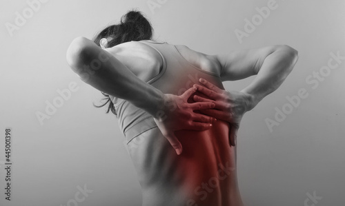 Young strong sporty woman suffering  and holding the hands her back, pain in the back, pain in the spine, highlighted in red.. The concept of medicine, massage, physiotherapy. Rear photo