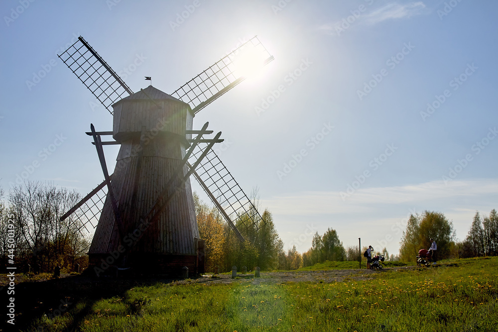 An old wooden windmill stands in a field near the forest