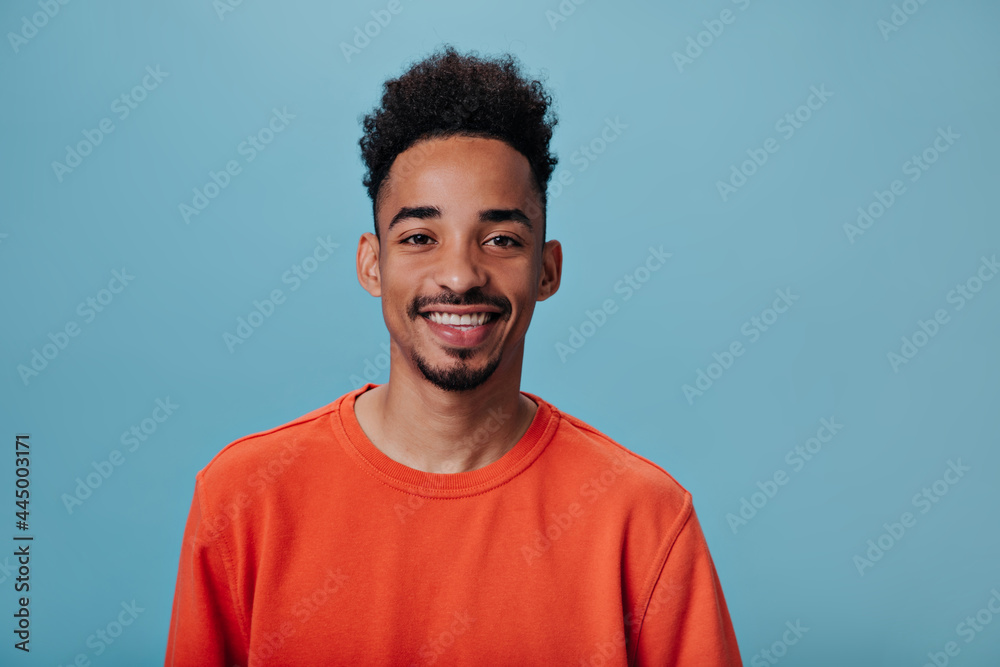 Portrait of brunett guy looks into camera on blue background. Brown-eyed man in red sweater widely smiling and looking into camera on isolated Portrait of brunett guy looks into camera on blue background. Brown-eyed man in red sweater widely smiling and looking into camera on isolated
