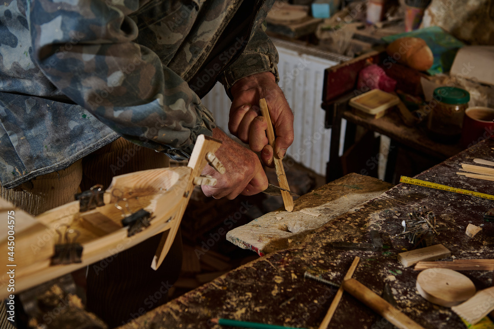 Carpenter using instruments to cut part of wood material to make wooden model of sailboat. Making handmade craft wooden toys. Close-up. Craftsman in action Carpenter using instruments to cut part of wood material to make wooden model of sailboat. Making handmade craft wooden toys. Close-up. Craftsman in action
