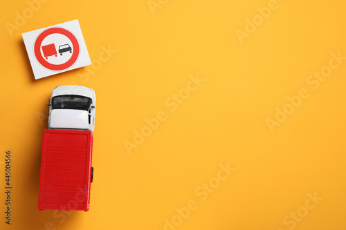 Toy lorry and road sign No Overtaking for on yellow background, flat lay
