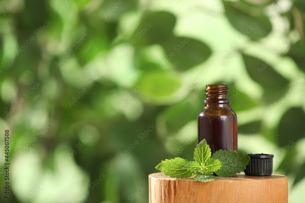 Glass bottle of nettle oil and leaves on wooden stump against blurred background, space for text