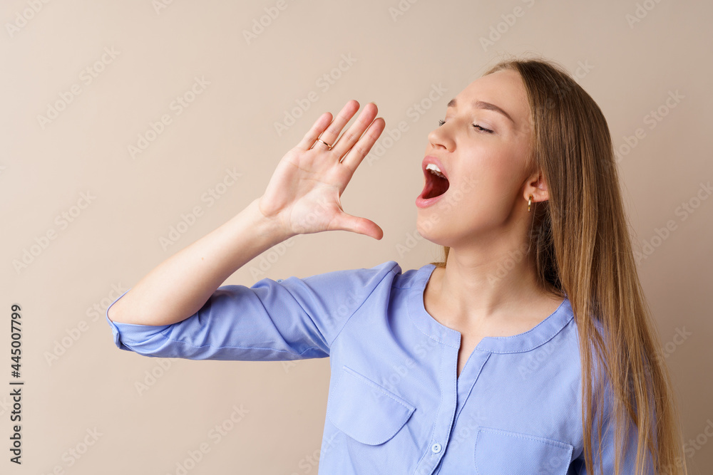 Young blonde woman screaming something loud, making announcement, against beige background Young blonde woman screaming something loud, making announcement, against beige background