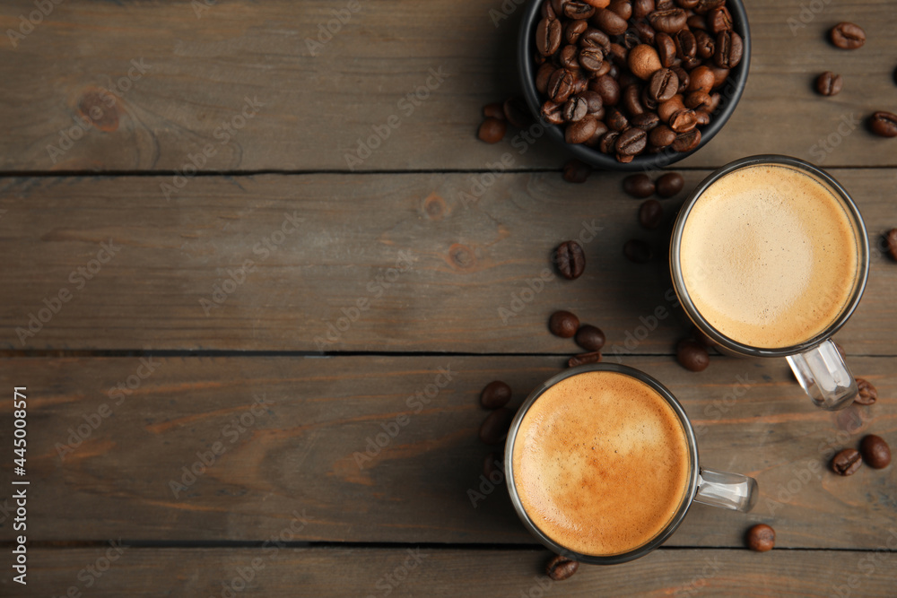 Cups of hot aromatic coffee and roasted beans on wooden table, flat lay. Space for text