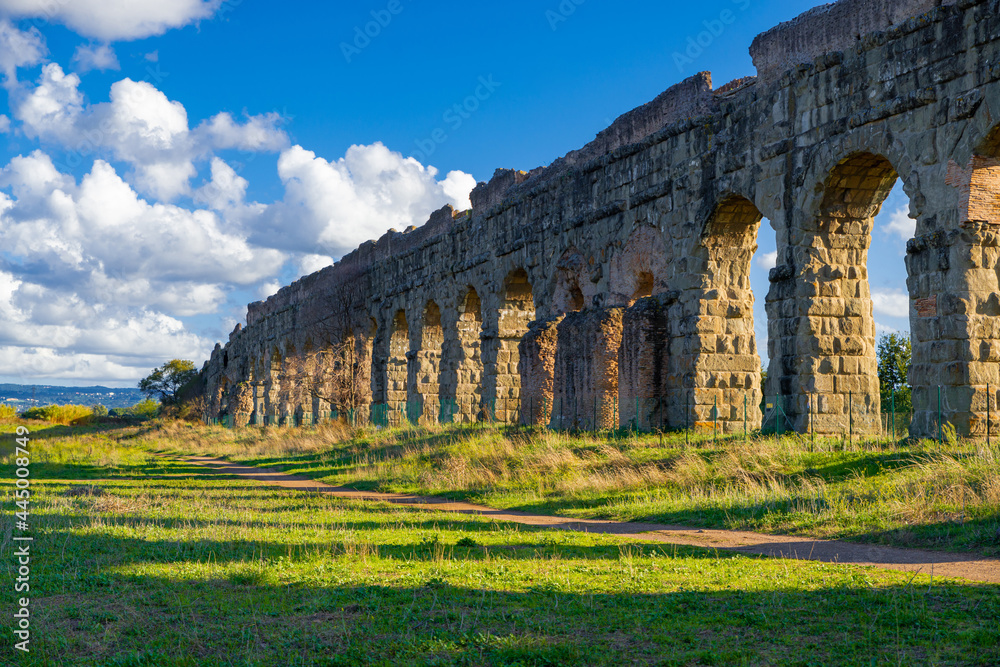 Park of the Aqueducts Rome, panorama of the arches of the Claudian Aqueduct with blue sky and clouds and shadows on the lawn. Archaeological area water system of ancient Rome. Via Appia Regional Park.