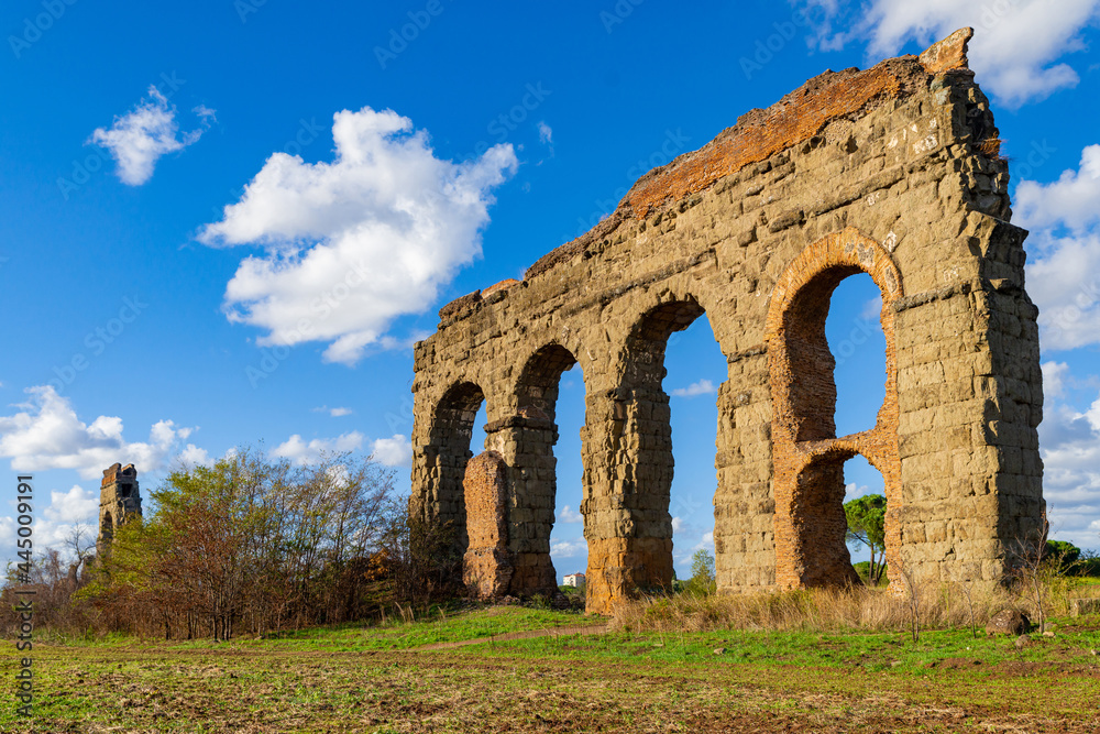 The Aqueduct Park in Rome, Italy. Ruins of the arches of the Claudius Aqueduct with blue sky and clouds. Public archaeological area, water system of ancient Rome. Regional Park Via Appia.Italy.