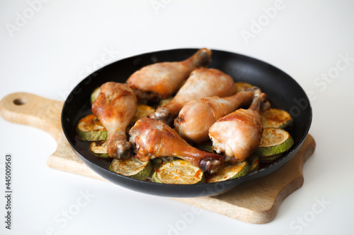 Fried chicken legs with zucchini slices in a frying pan on a wooden board