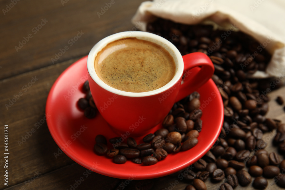 Obraz premium Cup of tasty coffee and beans on wooden table