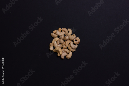 A handful of cashews on a black background. The nuts are folded in order. Background for the label. Light walnut.