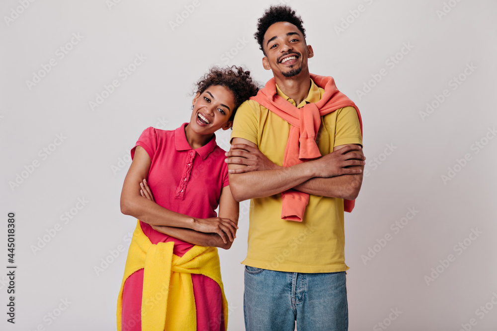 Smiling guy and woman looking into camera on white background. Cheerful man in yellow tee and cool girl in red dress smile on isolated Smiling guy and woman looking into camera on white background. Cheerful man in yellow tee and cool girl in red dress smile on isolated