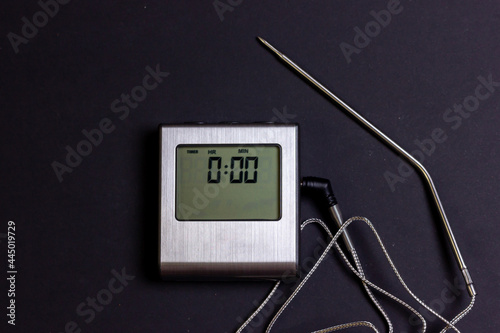 Kitchen thermometer with a probe on a black background. Electronic thermometer for measuring the temperature of food. Control of food preparation.