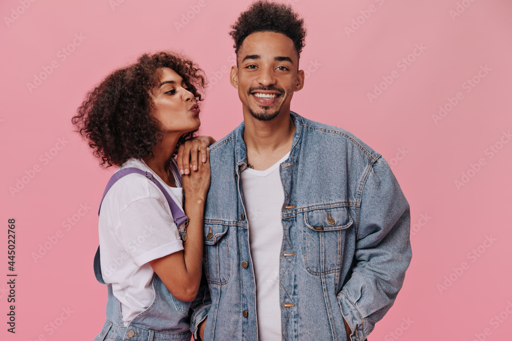 Curly girl wants to kiss her boyfriend on pink background. Close-up portrait of beautiful woman in white tee and man in denim jacket smiling on isolated Curly girl wants to kiss her boyfriend on pink background. Close-up portrait of beautiful woman in white tee and man in denim jacket smiling on isolated