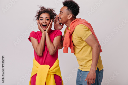 Couple gossip on isolated backdrop. Surprised woman in red sport-style dress and man in yellow shirt posing on white background