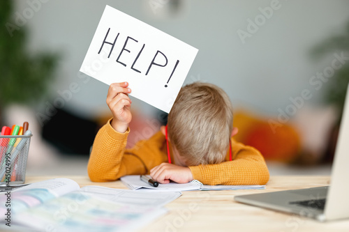 Foto unhappy tired child  boy student holds a sign HELP while doing homework at home