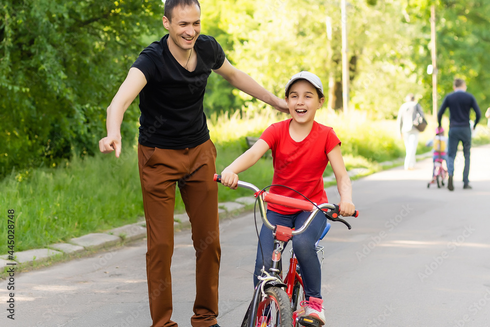 happy family father teaches child daughter to ride a bike in the Park in nature happy family father teaches child daughter to ride a bike in the Park in nature