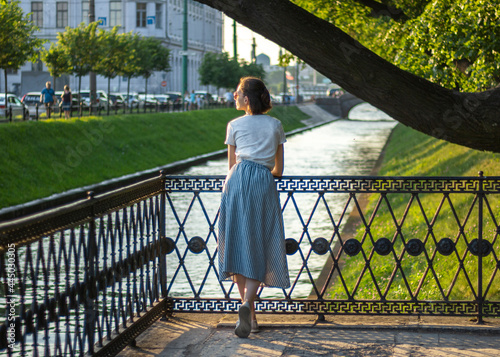 beautiful girl in a dress stands and looks at the river in the park back view