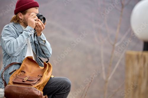 Young caucasian male travel with leather backpack on adventure taking photo on high mountain scenery, holding camera in hands, side view portrait. copy space