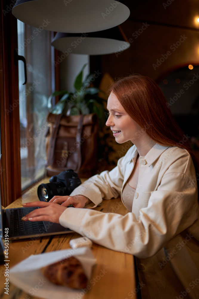 Hipster redhead caucasian woman traveler using laptop computer in cafe, working at coffee shop. freelance worker concept. Film color tone. Side view portrait. cozy atmosphere Hipster redhead caucasian woman traveler using laptop computer in cafe, working at coffee shop. freelance worker concept. Film color tone. Side view portrait. cozy atmosphere