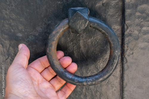 Hand holding an old ancient door knocker on a wooden door