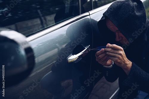 Car thief breaking into car with picklock or screwdriver. photo