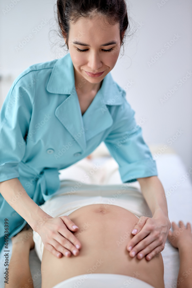 pregnant woman receiving tummy massage in spa center. Female patient is receiving treatment by professional therapist with beautiful hands. Body positive, harmony, healthy lifestyle. focus on masseur pregnant woman receiving tummy massage in spa center. Female patient is receiving treatment by professional therapist with beautiful hands. Body positive, harmony, healthy lifestyle. focus on masseur