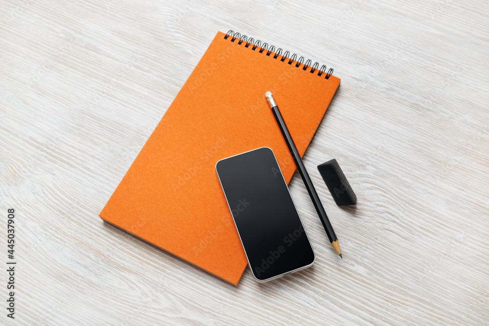Blank orange notepad, smartphone, pencil and eraser on light wood table background. Blank orange notepad, smartphone, pencil and eraser on light wood table background.