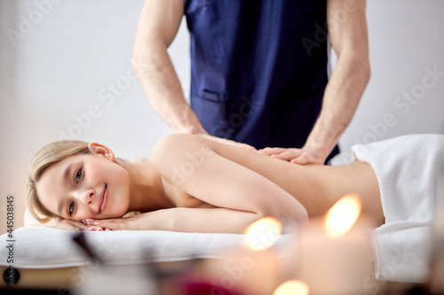 Charming Woman Lying On Belly Getting Spa Massage On Back By Male Masseur, Blonde Lady Of Caucasian Appearance Looking At Camera, Relaxed, Leisure Time, Spa Treatment Concept