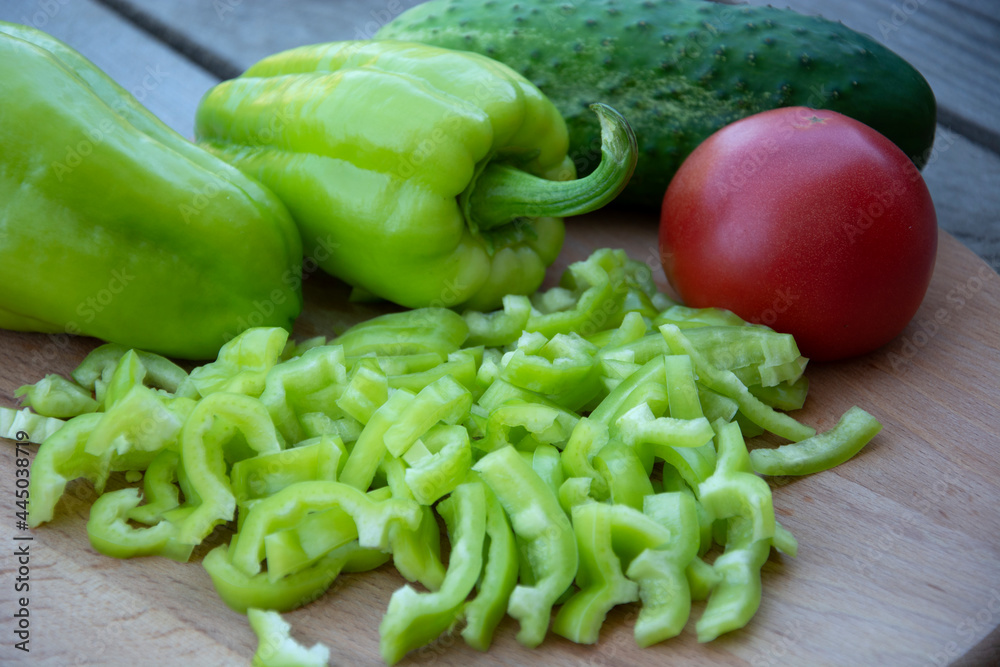 Red tomato, cucumber and bell peppers in strips lie on a wooden background. Harvest fresh vegetables from the garden. Red tomato, cucumber and bell peppers in strips lie on a wooden background. Harvest fresh vegetables from the garden.
