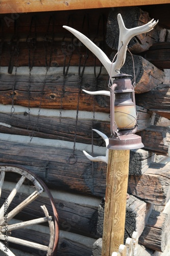 Fototapeta Naklejka Na Ścianę i Meble -  An Old Antique Lantern Hung From an Elk Antler in Front of a Log Cabin