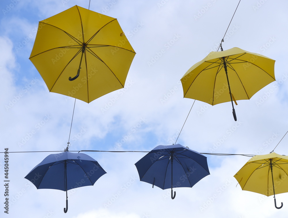 Vor blauem Himmel aufgespannte gelbe und blaue Regenschirme