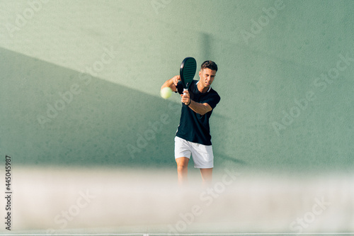 Man playing paddle tennis on an outdoor green paddle tennis court at the sunset © Henko Studio